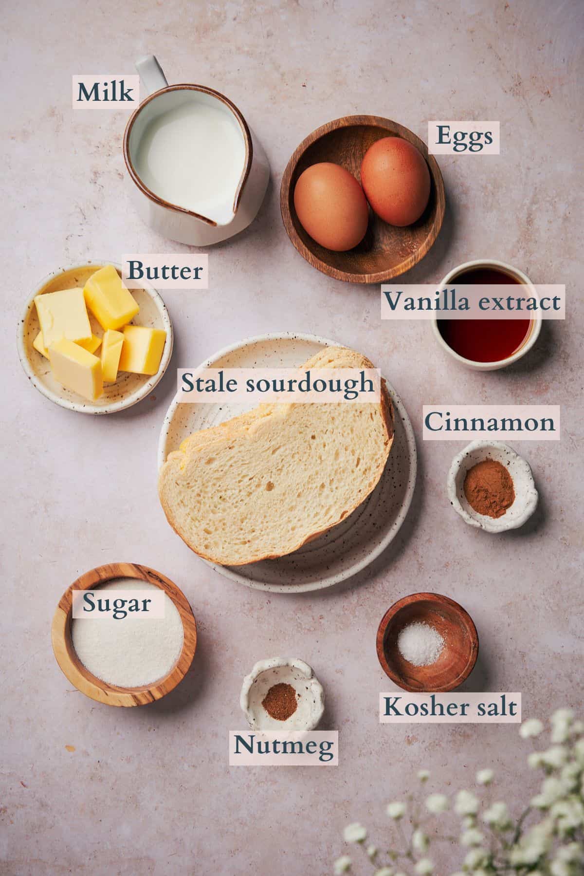 Ingredients for sourdough french toast laid out on an elegant background in various bowls and containers.