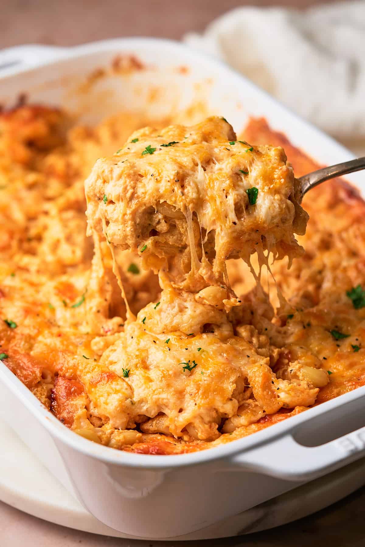Large spoonful of cheesy Southern baked mac and cheese being pulled from a casserole dish, with strings of cheese pulling. 