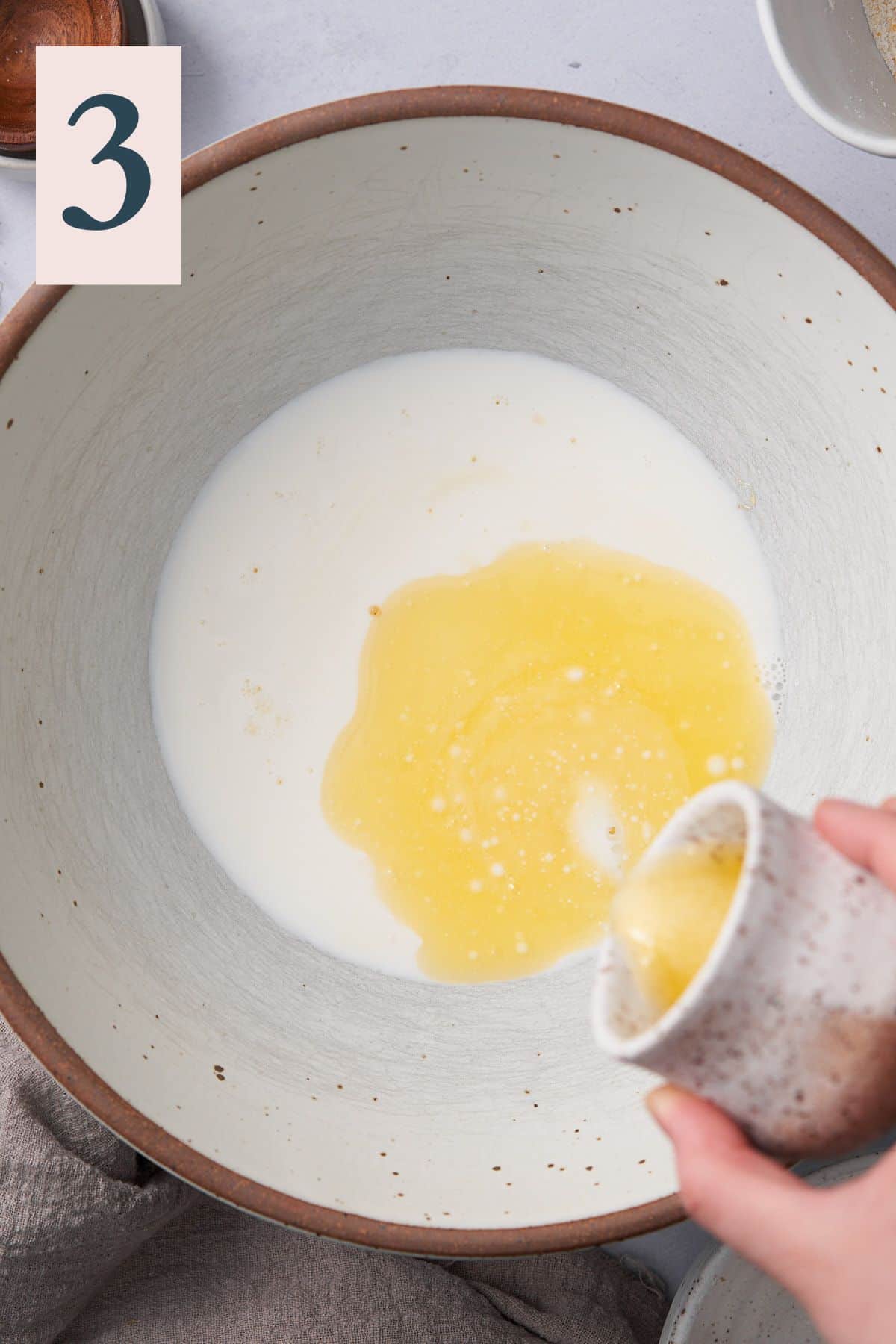 hand pouring melted butter into a large bowl with milk. 