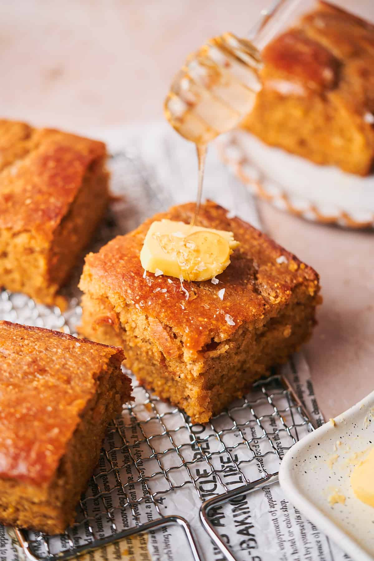 squares of sweet potato cornbread on a potato grater with a pat of butter on top, with a honey dripper drizzling honey onto the cornbread. 