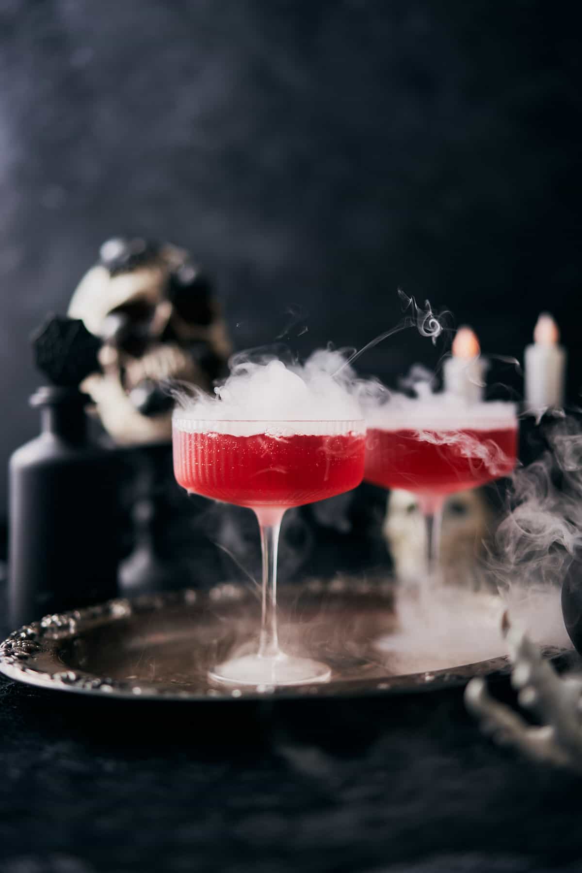 Vampire's kiss cocktail with bubbling mist and spooky decor in the background.